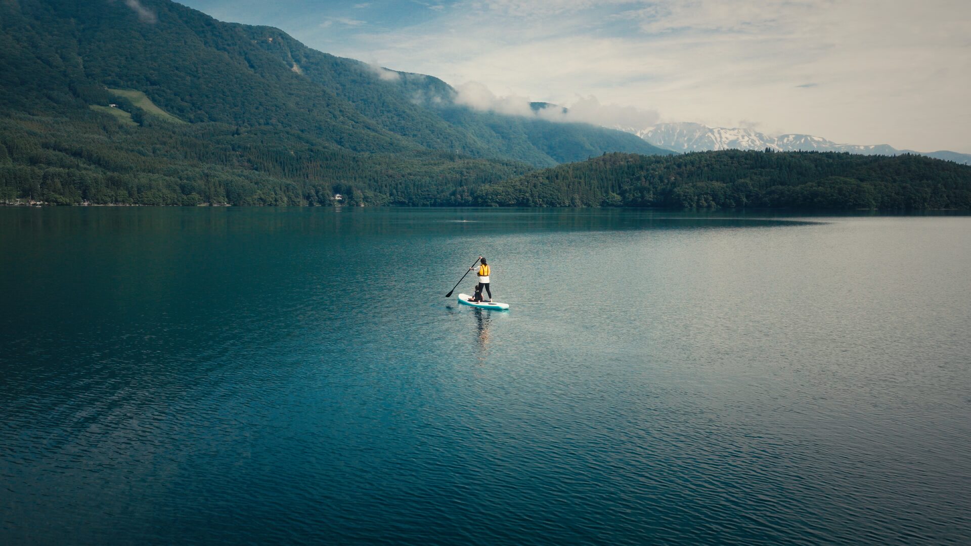 paddleboarding on Lake Aoki by Lakeside Cafe Ao with forested mountains and snow-capped peaks in Hakuba, Japan