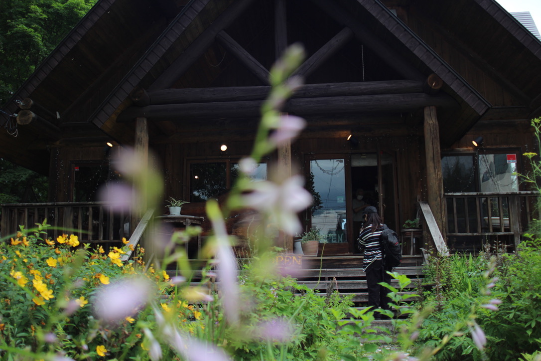 40F67743-CB9D-40C5-BDAB-2EF7F60893D2_1_105_c Entrance to Gravity Worx Hakuba, a rustic log cabin restaurant surrounded by seasonal alpine flowers and lush greenery near Hakuba Station.