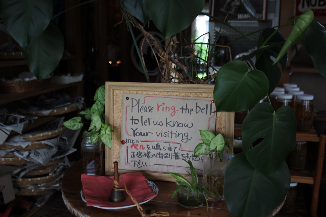9C430D31-E15E-4ECE-AD4A-897143DDE05E_1_105_c Vintage-style welcome sign written in Japanese and English at Gravity Worx Hakuba asking guests to ring the bell, surrounded by lush indoor plants and rustic wooden décor — a charming touch at this hidden mountain café known for its warm hospitality and homemade dishes.