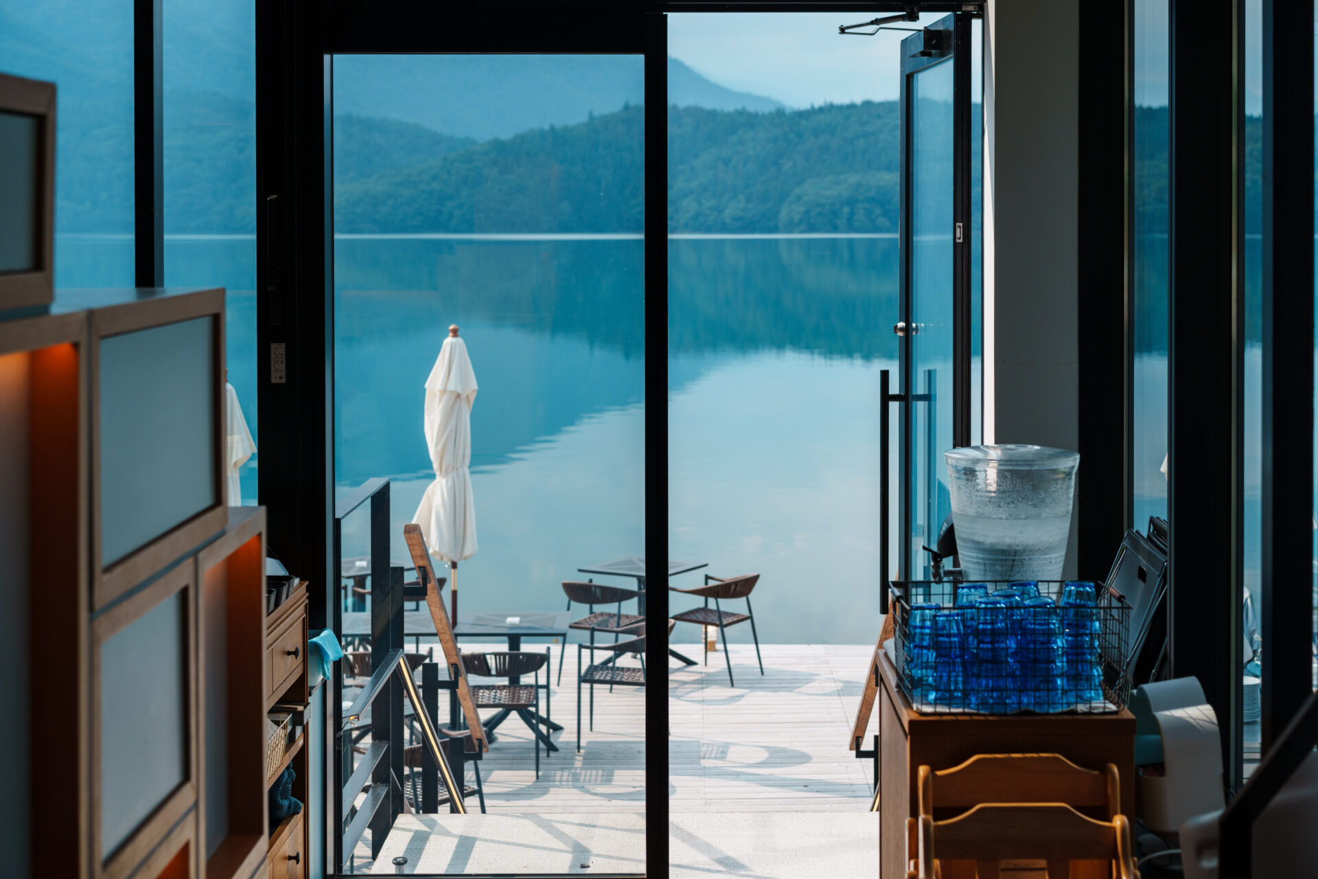 Café interior with glass doors opening to a lakeside terrace overlooking Lake Aoki in Hakuba, Japan