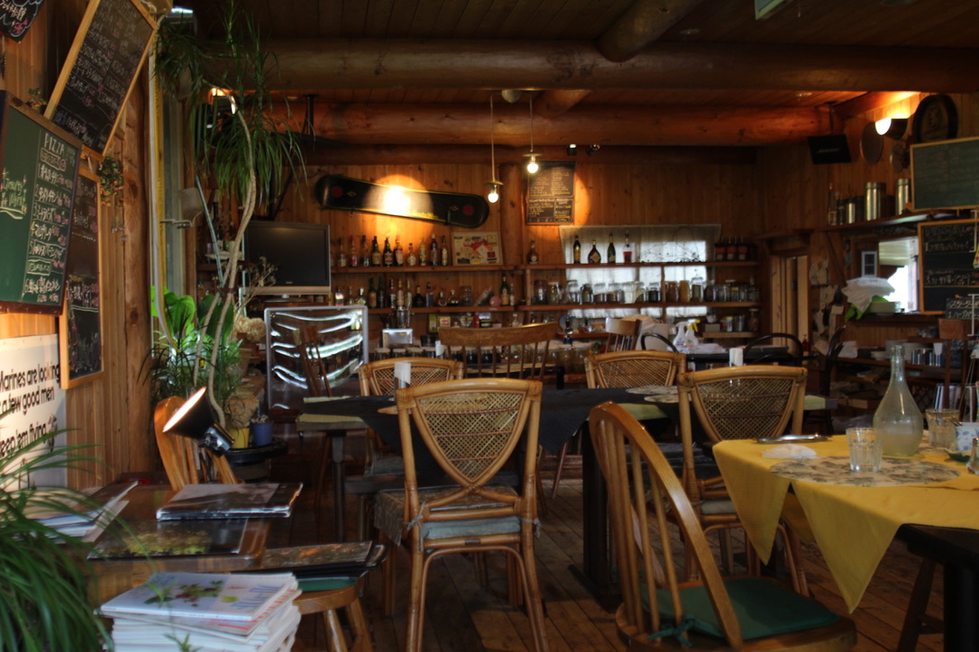 D7966B06-2859-4ACF-A5D6-314BF4877909_1_105_c Cozy rustic café in Hakuba with wooden log cabin interior, vintage rattan chairs, vibrant table settings, lush greenery, and a well-stocked bar — ideal for relaxing après-ski meals or a warm countryside dining experience in the Japanese Alps.