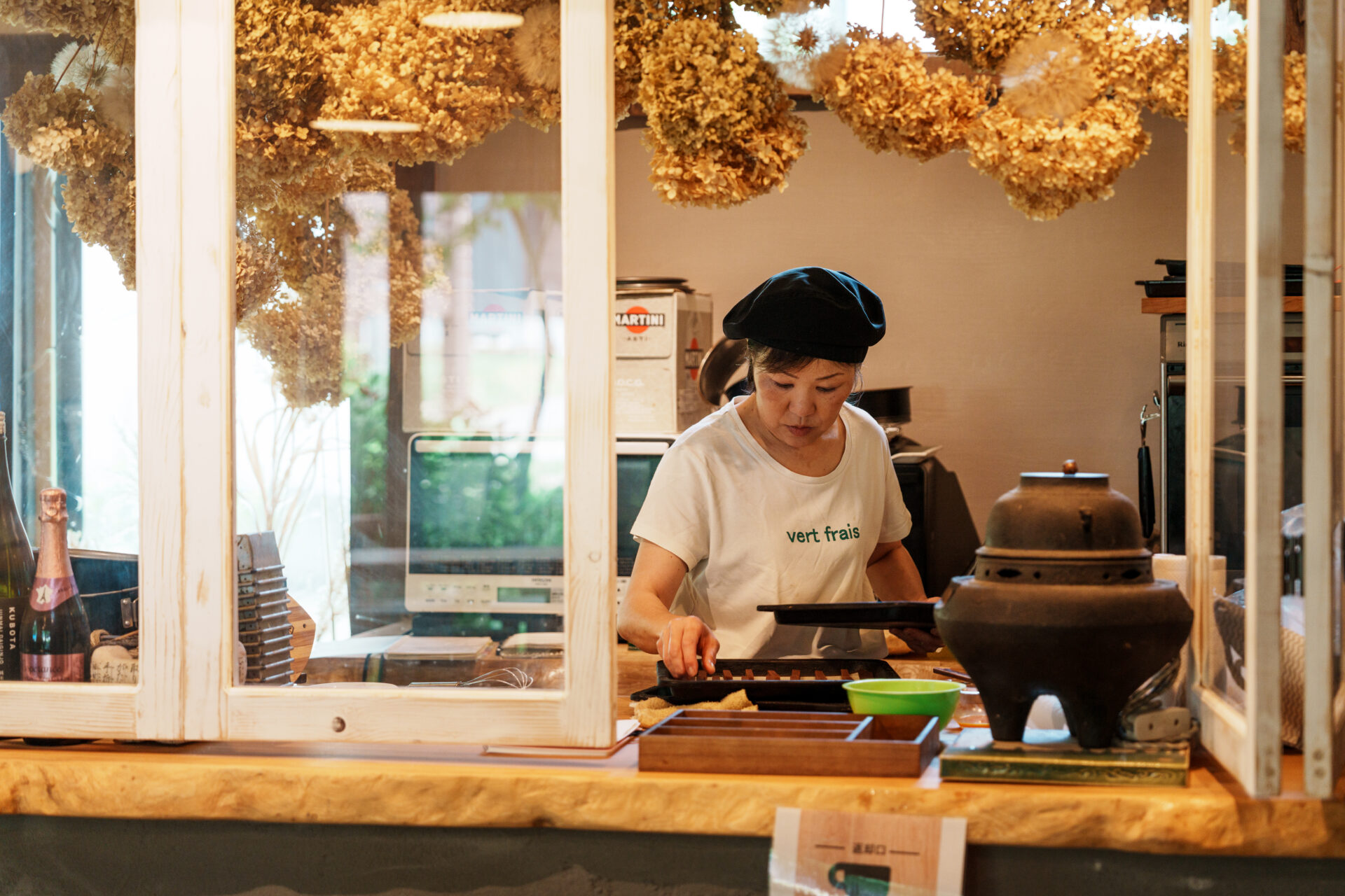 Cafe staff preparing food behind wooden counter decorated with hanging dried flowers