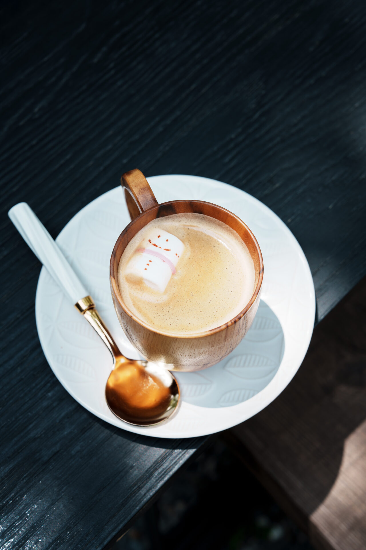 Latte served in wooden cup with cute marshmallow snowman on white saucer