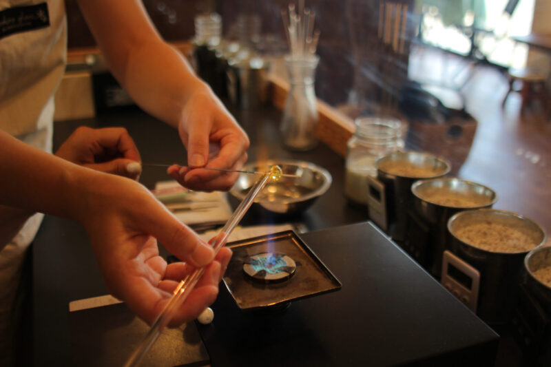 Close-up of hands shaping molten glass over a flame torch during a glass bead workshop at Kira Kira Glass in Nagano, Japan.