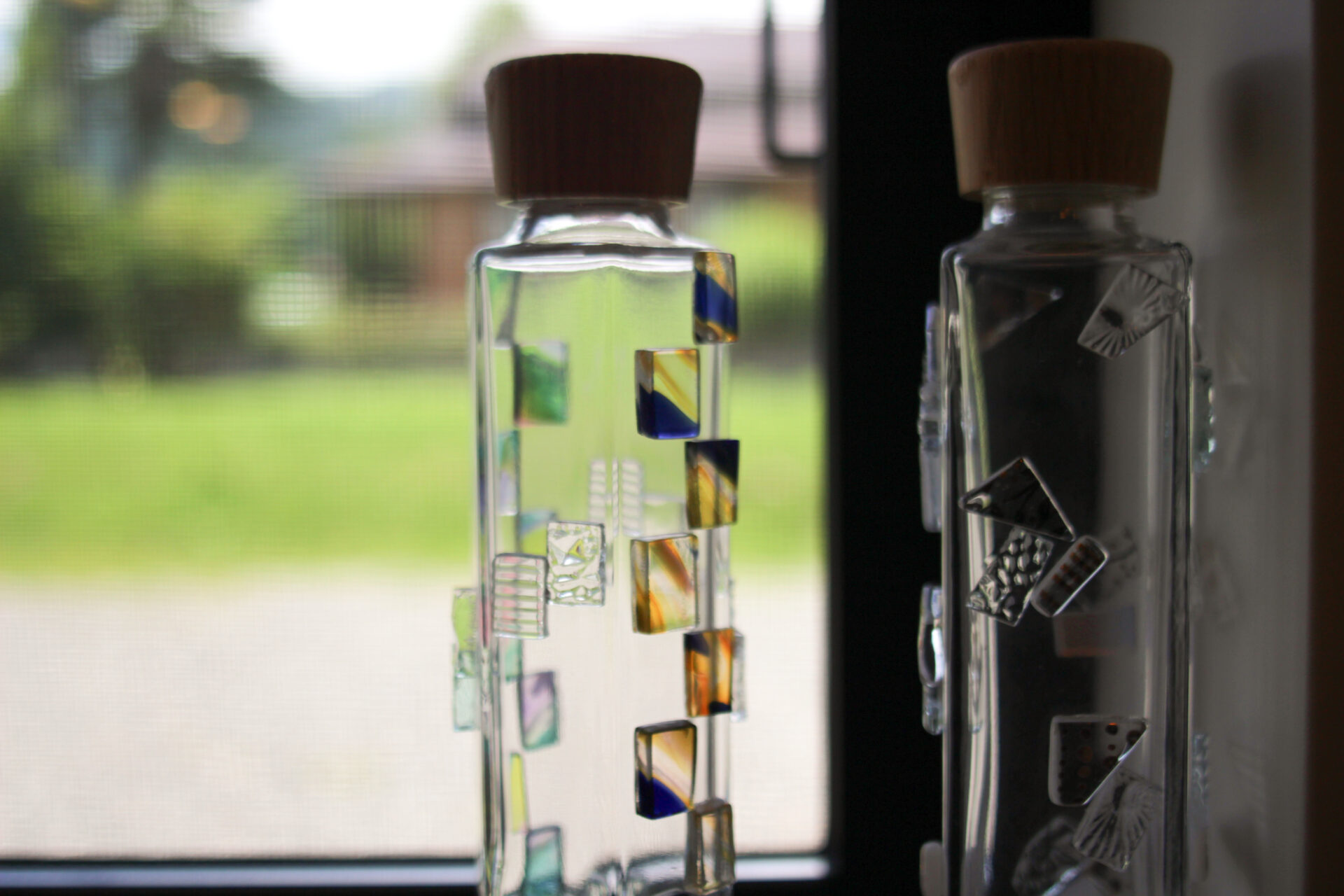 Decorative glass bottles with colorful handmade glass tiles on display at Kira Kira Glass in Hakuba, Nagano—available for purchase as unique Japanese souvenirs.