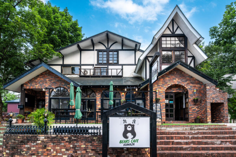 Exterior of Bears Café Kumaza in Echoland, Hakuba, Japan—brick and timber chalet-style building with outdoor seating, surrounded by greenery.
