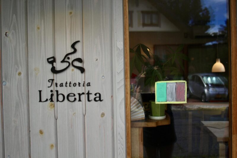 Vintage-style welcome sign written in Japanese and English at Gravity Worx Hakuba asking guests to ring the bell, surrounded by lush indoor plants and rustic wooden décor — a charming touch at this hidden mountain café known for its warm hospitality and homemade dishes.