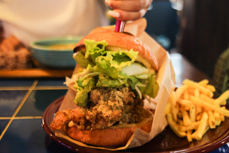 Towering chicken burger with avocado, lettuce, and herbs served at Sounds Like Café Hakuba, known for the biggest burgers in Echoland.