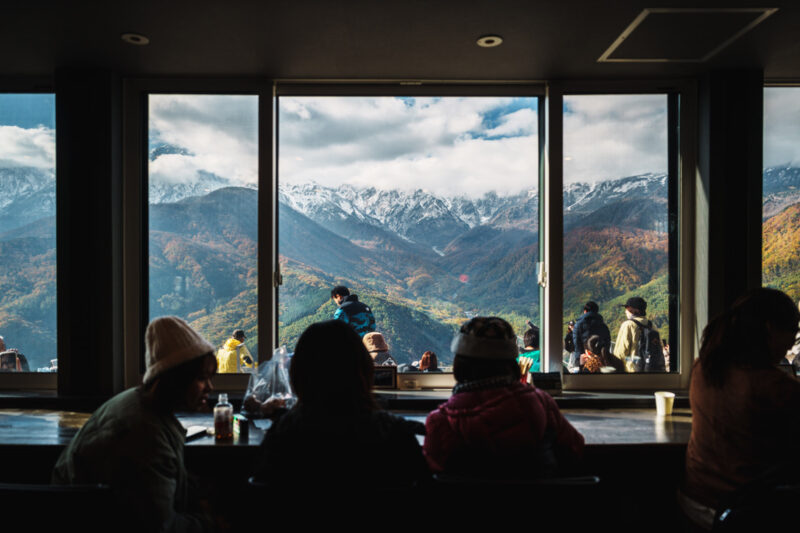 Hand holding a CHAVATY HAKUBA iced matcha latte with mountain views in the background — premium tea latte specialty café in the Japanese Alps, offering scenic outdoor experiences and artisanal drinks made with carefully selected tea leaves.